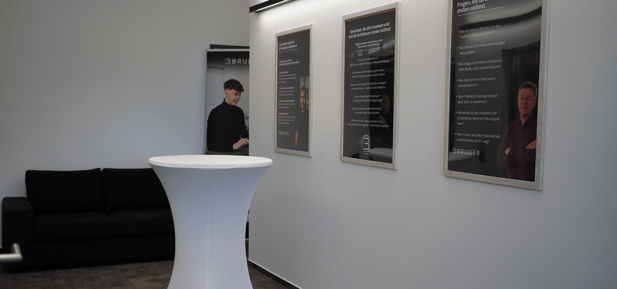 Foto einer Büroszene mit Personen im Gespräch und Wandpostern, symbolisiert praxisnahe Arbeit und reale Einblicke aus dem E-Commerce-Alltag