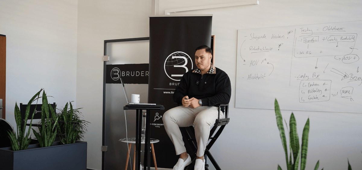 Dozent sitzt vor einer Meta-Ads Trainingskulisse mit Whiteboard und BRUDER-Branding und erklärt, wie datenbasierte Entscheidungen Kampagnenergebnisse messbar verbessern